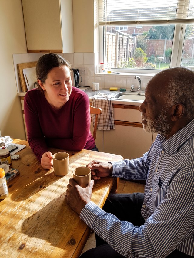 An older man and his caregiver sharing morning coffee at a kitchen table
